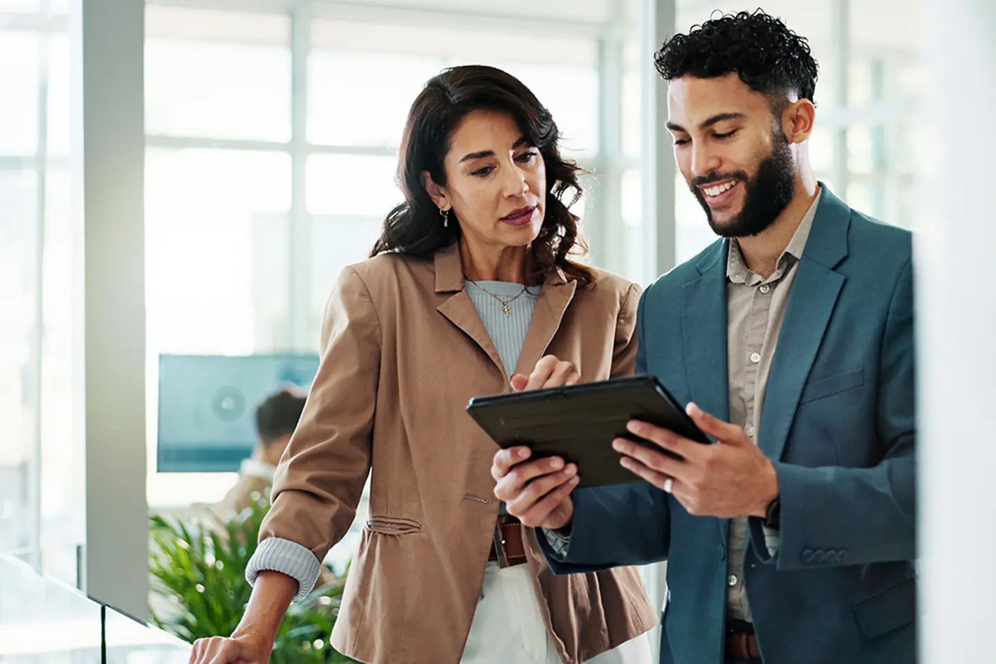 Two professionals discuss office work using a tablet as a reference.